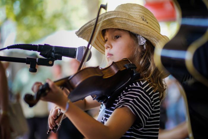 A young girl in a straw hat plays the fiddle on Peel Street