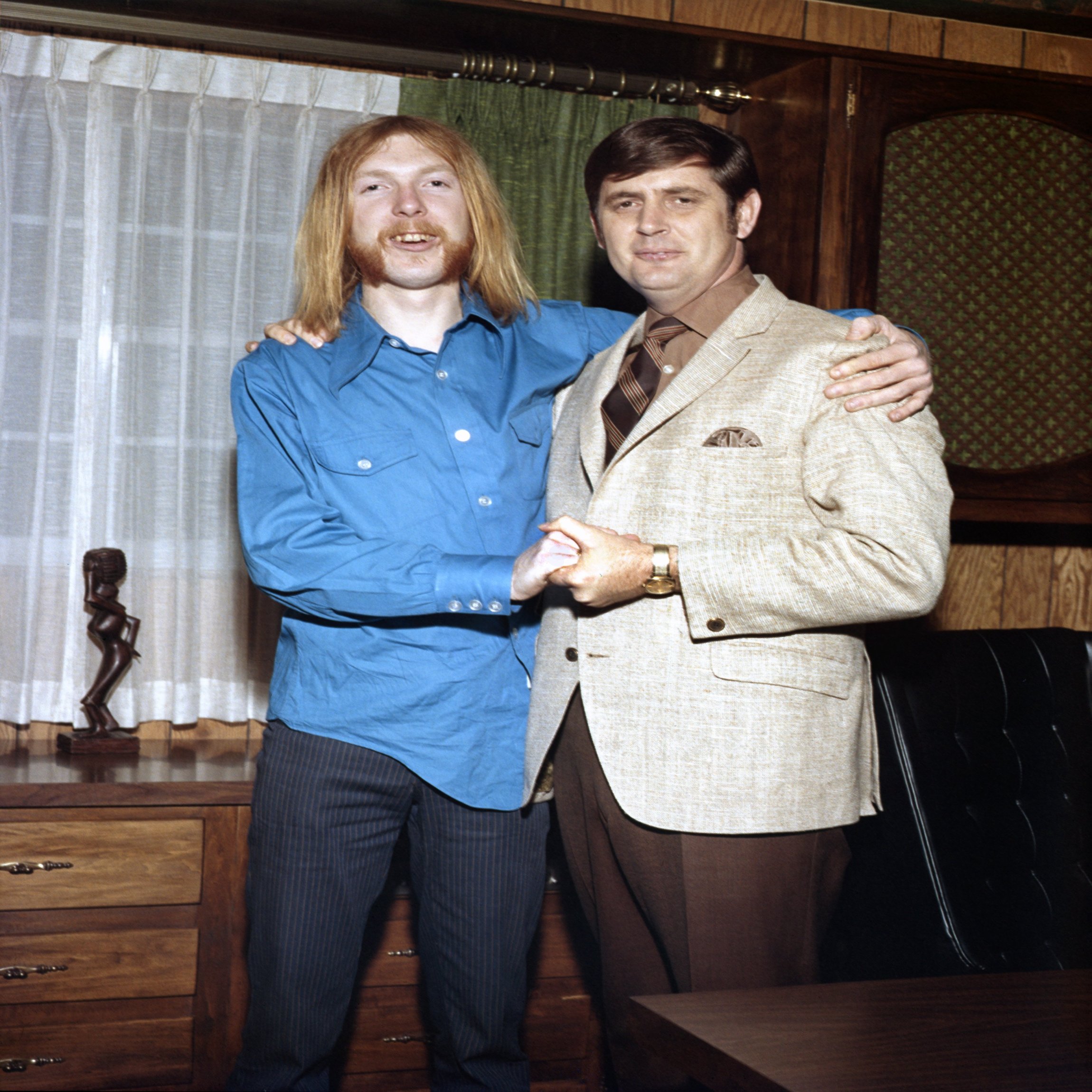 MUSCLE SHOALS, AL - 1968: Songwriter and producer Rick Hall (right) signs session guitarist Duane Allman (left) to a contract in his office at FAME Studios in 1968 in Muscle Shoals, Alabama. (Photo by House Of Fame LLC/Michael Ochs Archives/Getty Images)