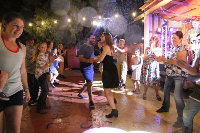 Two people dance surrounded by a crowd as it rains.